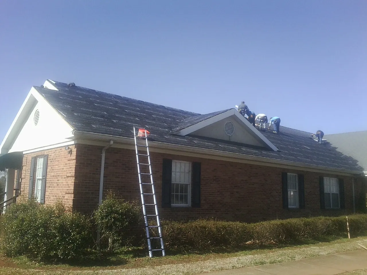 Crew tearing shingles off a brick ranch roof with a ladder set — Metal Roof Repair work by our crew in Paulina