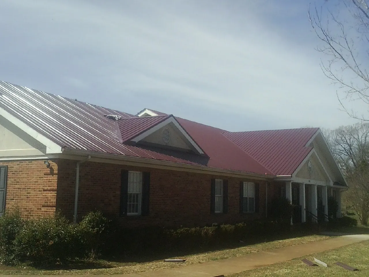 Red metal roof with gabled entries on a long brick building, from a Hail Damage Roof Repair job in Paulina