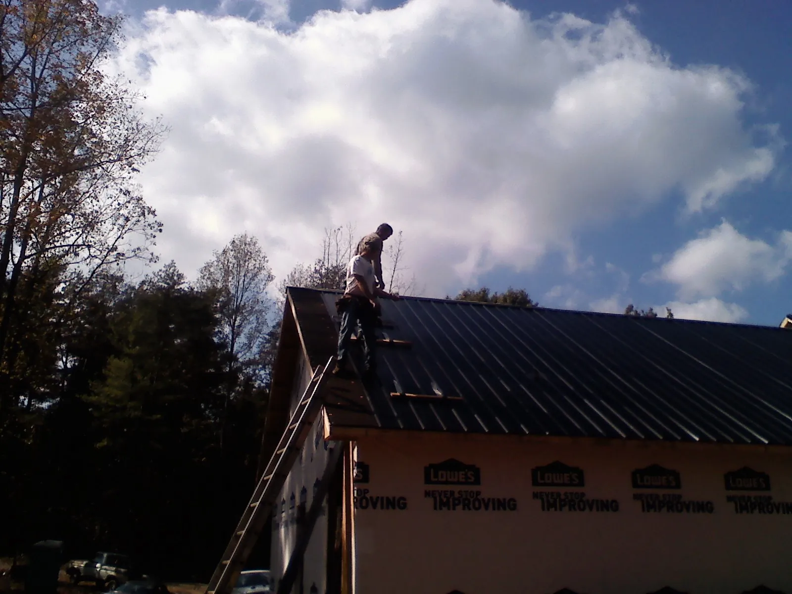 Roofer fastening dark metal panels high against a cloudy sky, from a Roof Inspection job in Paulina