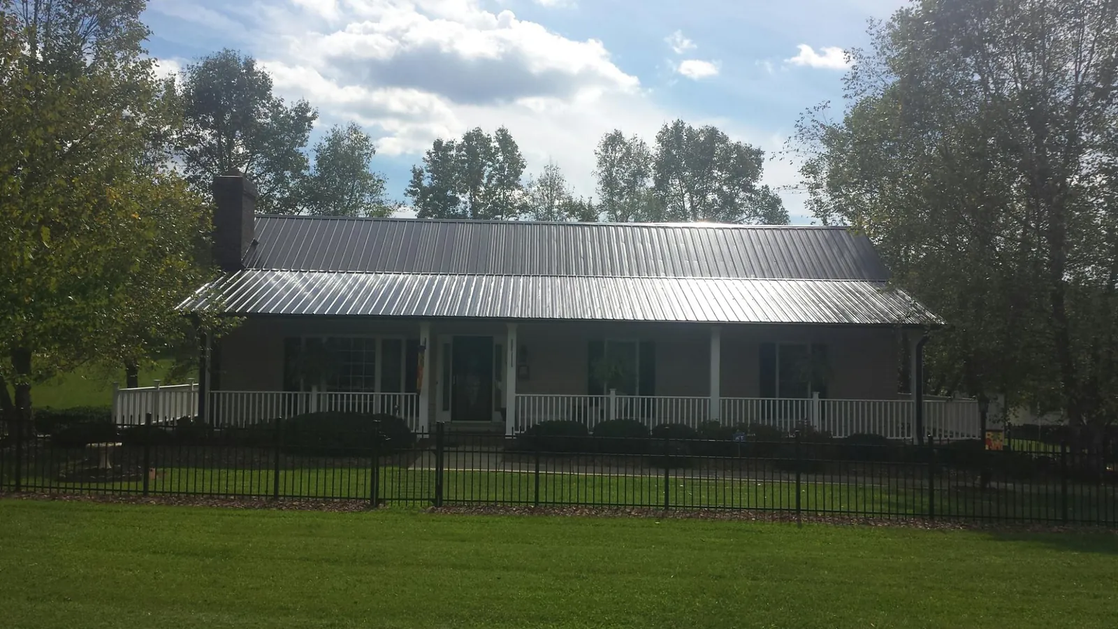 Gray metal roof on a brick ranch with a full width front porch — Gutter Guard Installation work by our crew in Paulina