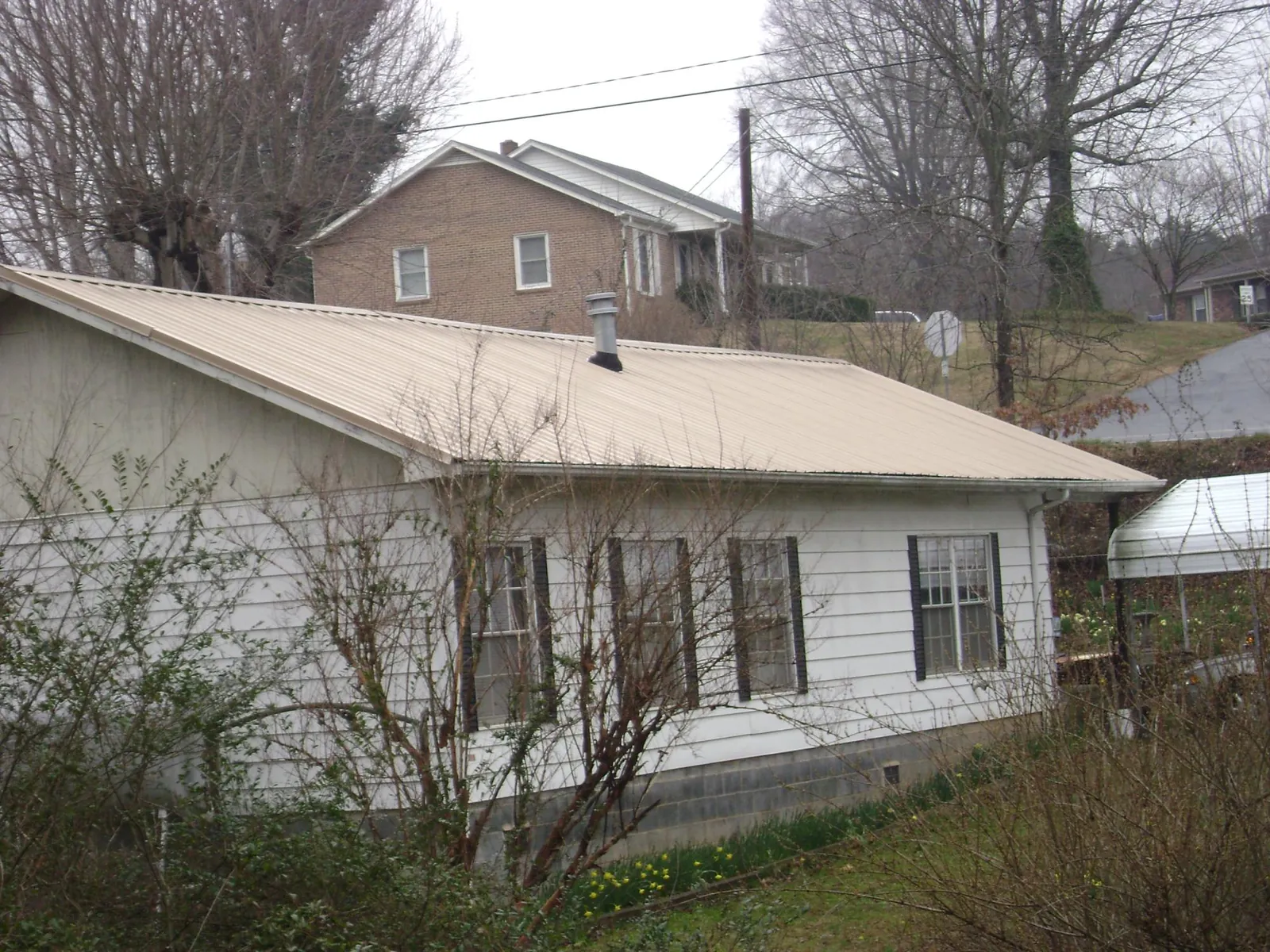 Tan metal roof on a white sided house set into a hillside — Commercial Roofing by Roofing Brothers in Paulina
