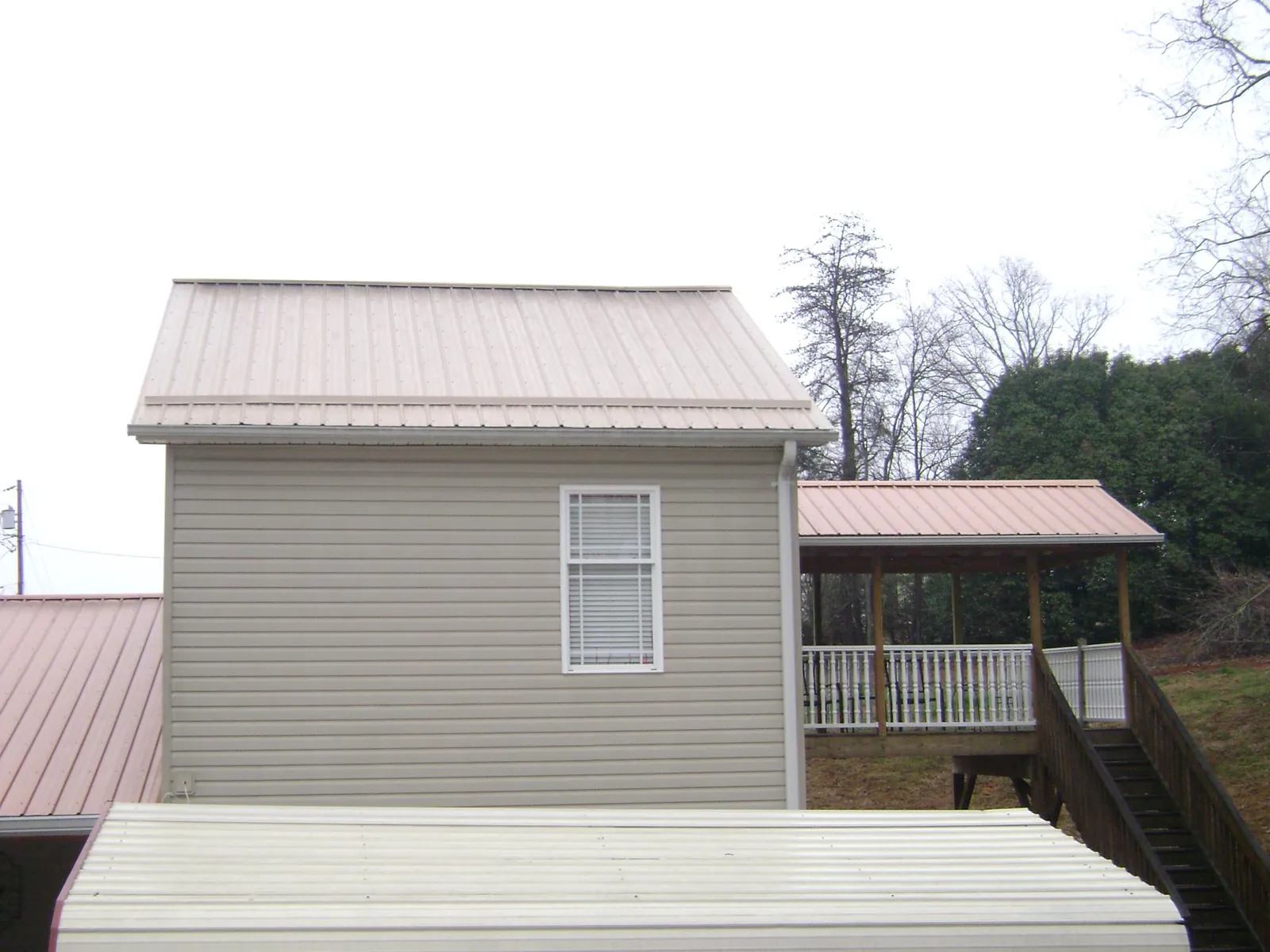 Tan metal roofs on a two story addition and attached porch, from a Roof Replacement job in Paulina